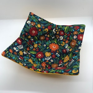 May include: A square bowl with a floral print in shades of red, orange, yellow, blue, and green on a dark blue background. The bowl has a yellow border.