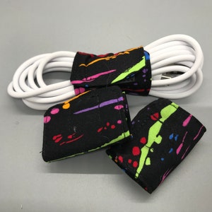 May include: Three colorful fabric cord organizers with a black background and a white cord wrapped around them.