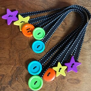 May include: A set of six colorful button bookmarks with black and white ribbon. The buttons are green, blue, orange, yellow, and purple. The ribbon has white polka dots.