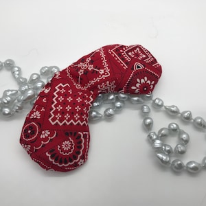 Puede incluir: Una m&aacute;scara para los ojos de tela de bandana roja con un patr&oacute;n paisley blanco y negro, descansando sobre una hebra de perlas gris plateado.