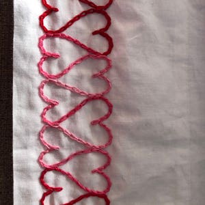May include: A white fabric with a row of red and pink embroidered hearts.