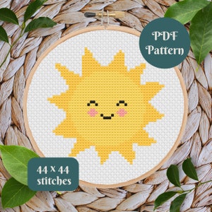 May include: A cross-stitch pattern of a smiling yellow sun with pink cheeks, set in a wooden embroidery hoop. The text "PDF Pattern" is in a green circle. The text "44 x 44 stitches" is in a green rectangle.