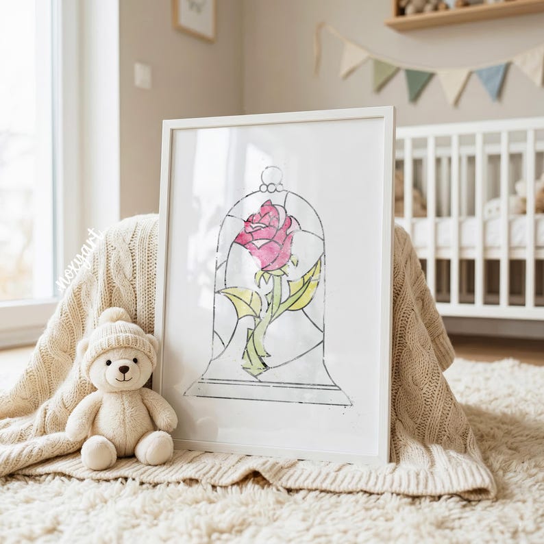 May include: A framed watercolor print of a pink rose in a glass bell jar. The artwork is in a white frame and rests on a cream-colored blanket. A small teddy bear wearing a hat sits nearby. The background includes a crib and a window.