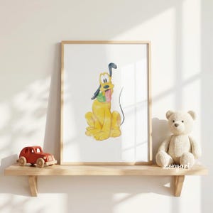 Op de afbeelding: Waterverfprint van Pluto, een gele cartoonhond, in een houten lijst. Het kunstwerk wordt tentoongesteld op een houten plank met een rode speelgoedauto en een teddybeer. De print toont Pluto met zijn tong uit.