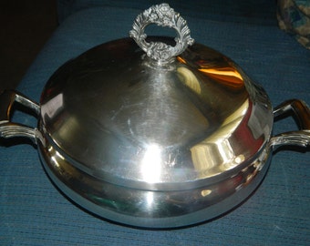 Può includere: Un piatto da portata in argento con coperchio e due manici. Il coperchio ha un motivo floreale decorativo sul pomo.