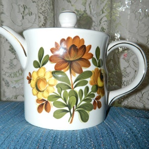 May include: White ceramic teapot with a floral design featuring brown, yellow, and green flowers. The teapot has a lid and a handle.
