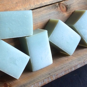 May include: Five bars of light blue soap arranged in a wooden crate. The soap is handmade and has a natural, earthy look.