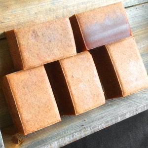 Puede incluir: Seis barras de jabón hechas a mano en una caja de madera. El jabón es de color marrón claro y tiene una textura rugosa.