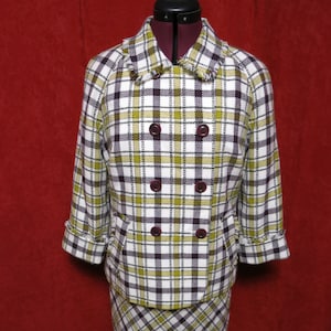 Puede incluir: Un conjunto de chaqueta y falda de cuadros blancos, amarillos y marrones. La chaqueta tiene cierre de doble botonadura y cuatro botones. La falda es de largo hasta la rodilla.