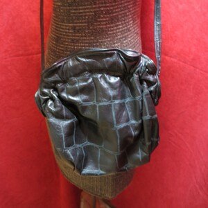 May include: A black leather crossbody bag with a crocodile-embossed pattern. The bag has a long strap and a rounded shape.