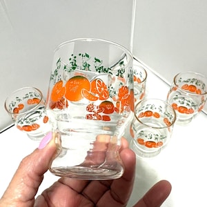 May include: Set of six vintage clear glass juice glasses. Each glass features a design of orange fruit and green leaves. The glasses are a short, rounded shape with a flared base, perfect for serving juice or cocktails.