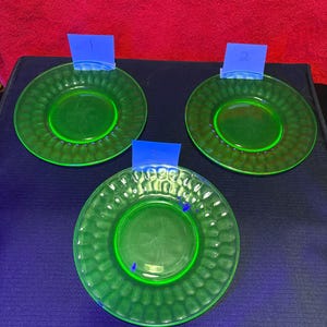 Può includere: Tre piatti circolari in vetro verde traslucido caratterizzati da un motivo testurizzato a fossette lungo il bordo esterno. Ogni piatto è accompagnato da una piccola etichetta di carta blu contrassegnata con i numeri 1, 2 e 3, che indica i singoli oggetti.