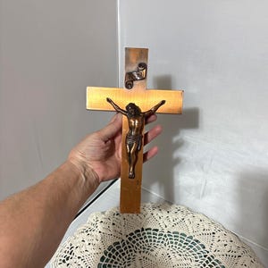 Puede incluir: Un crucifijo de madera con una figura de bronce de Jesucristo. La cruz es de madera marrón claro con una figura de bronce de Jesús. La figura está detallada con los brazos extendidos. Una inscripción con las letras INRI está en la parte superior.