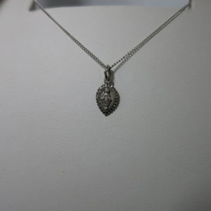 May include: A silver chain necklace with a small silver pendant featuring a detailed image of the Virgin Mary.