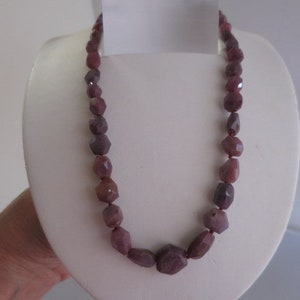 May include: A necklace made of faceted, dark pink gemstone beads. The beads are strung on a clear thread and are approximately 1/2 inch in diameter.