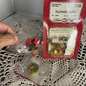 May include: Miniature flower pots and accessories, including a red and green potted plant, and a small container of greenery. The packaging reads "Flower Pots" and "Fibre Craft". The flower pots are 1/2 inch in size.