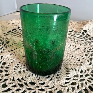 Op de afbeelding: Een groene tumbler van craquelé glas. Het glas heeft een getextureerd oppervlak met een netwerk van fijne scheuren. De tumbler is cilindrisch met een licht uitlopende rand. De kleur is een levendig, diep groen.