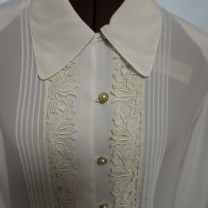 May include: A white sheer blouse with a lace trim and pearl buttons. The blouse has a classic collar and long sleeves.