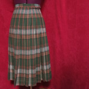 May include: A long green, brown and white plaid skirt with pleats. The skirt is on a mannequin and the background is red.