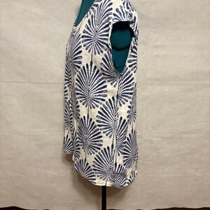 K&ouml;nnte beinhalten: Ein &auml;rmelloses Oberteil mit wei&szlig;em Hintergrund und einem sich wiederholenden marineblauen Blattmuster. Das Oberteil hat einen Rundhalsausschnitt und wird auf einer Schaufensterpuppe pr&auml;sentiert. Der Stoff scheint ein leichtes Material zu sein.