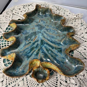 Könnte beinhalten: Ein handgefertigtes Keramik-Serviertablett und ein kleines Schüssel-Set. Das Tablett hat eine Blattform mit gewelltem Rand, glasiert in Blau- und Brauntönen. Die kleine Schüssel hat die gleiche Farbe. Ein einzigartiges Stück.