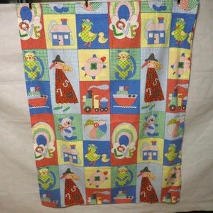 Puede incluir: Una colorida tela de patchwork con cuadrados ilustrados. Los cuadrados muestran imágenes de casas, patos, osos de peluche, barcos y una figura con sombrero. La tela tiene un esquema de color rojo, azul, amarillo y verde.