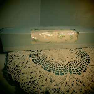 May include: A blue and white floral patterned gift wrap is rolled up and packaged in a blue box. The box is sitting on a white crocheted doily.