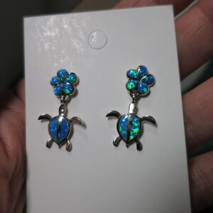 Könnte beinhalten: Ein Paar silberne Ohrringe mit blauen Opal-Blüten- und Schildkrötenanhängern.