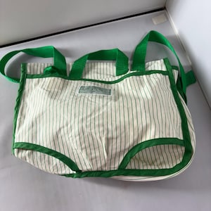 May include: White tote bag with vertical green stripes and green trim. The bag has green handles and a small rectangular tag. The bag is made of a soft fabric.