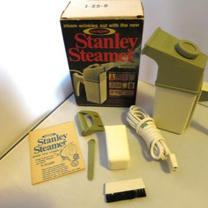 May include: A vintage Stanley Steamer set, including the steamer unit, accessories, and original box. The box features the text "steam wrinkles out with the new Stanley Steamer". The steamer is a light green and white color.
