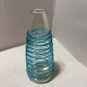 May include: A clear glass vase with a tapered neck and a wide base, featuring a continuous bright blue glass coil wrapped in a spiral pattern around the exterior of the body from the base up to the neck, creating a distinct textured appearance.