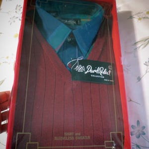 May include: A boxed shirt and sleeveless sweater set. The shirt has a blue and green plaid pattern collar. The sleeveless sweater is a deep red with vertical ribbing. The packaging is red with gold accents. The label reads "David Robert Collection".