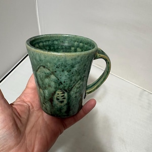 May include: A white ceramic mug with a black handle and the text "But First, Coffee" in a black, bold font. The mug is sitting on a white surface. The mug is approximately 4 inches tall.