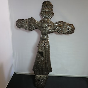 May include: A metal crucifix with a detailed design. The figure of Jesus is depicted with a crown of thorns and a flowing robe. The cross is decorated with intricate patterns and has a textured surface.