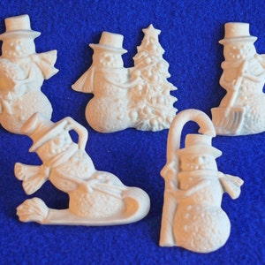 May include: Five white ceramic snowman ornaments. The snowmen are in various poses, including holding a candy cane, a shovel, and a Christmas tree.