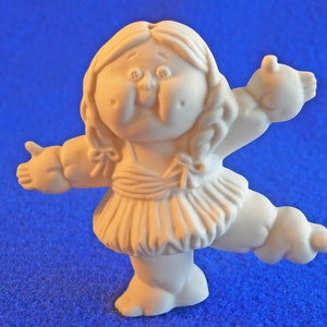 May include: A white ceramic figurine of a Cabbage Patch Kid doll wearing a dress and holding out one arm. The doll has a round face with rosy cheeks and a sweet expression.