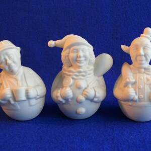 May include: Three white ceramic figurines of people with whimsical expressions. The figurine on the left is wearing a hat and holding a mug. The middle figurine is wearing a hat and holding a lollipop. The figurine on the right is wearing a hat and holding a flower.