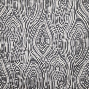 May include: A fabric with a repeating pattern of concentric, oval shapes in shades of gray and white, resembling the cross-section of a tree trunk. The design has a natural, organic feel, suitable for home decor or apparel.