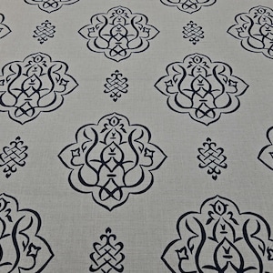 May include: A beige fabric with a repeating pattern of black, intricate, floral designs. The design is symmetrical and has a traditional, ornate look.