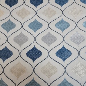 May include: A white fabric with a repeating pattern of blue, beige, and gray teardrop shapes. The teardrops are outlined in black and connected by a black lattice pattern.