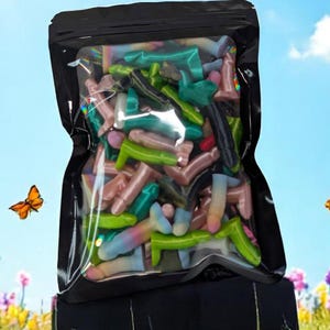 Puede incluir: Una bolsa negra resellable llena de coloridos títeres de dedos de silicona. La bolsa está sentada sobre hierba verde con un cielo azul brillante y nubes blancas en el fondo.