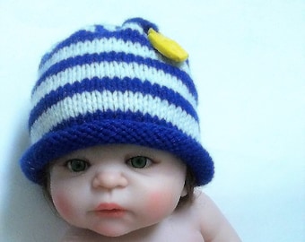 May include: A baby doll wearing a blue and white striped knitted hat with a yellow flower embellishment. The doll is wearing a diaper and has a realistic appearance.