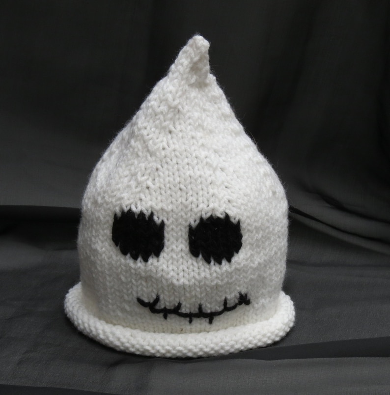 May include: White knitted ghost hat with black embroidered eyes and a stitched mouth.