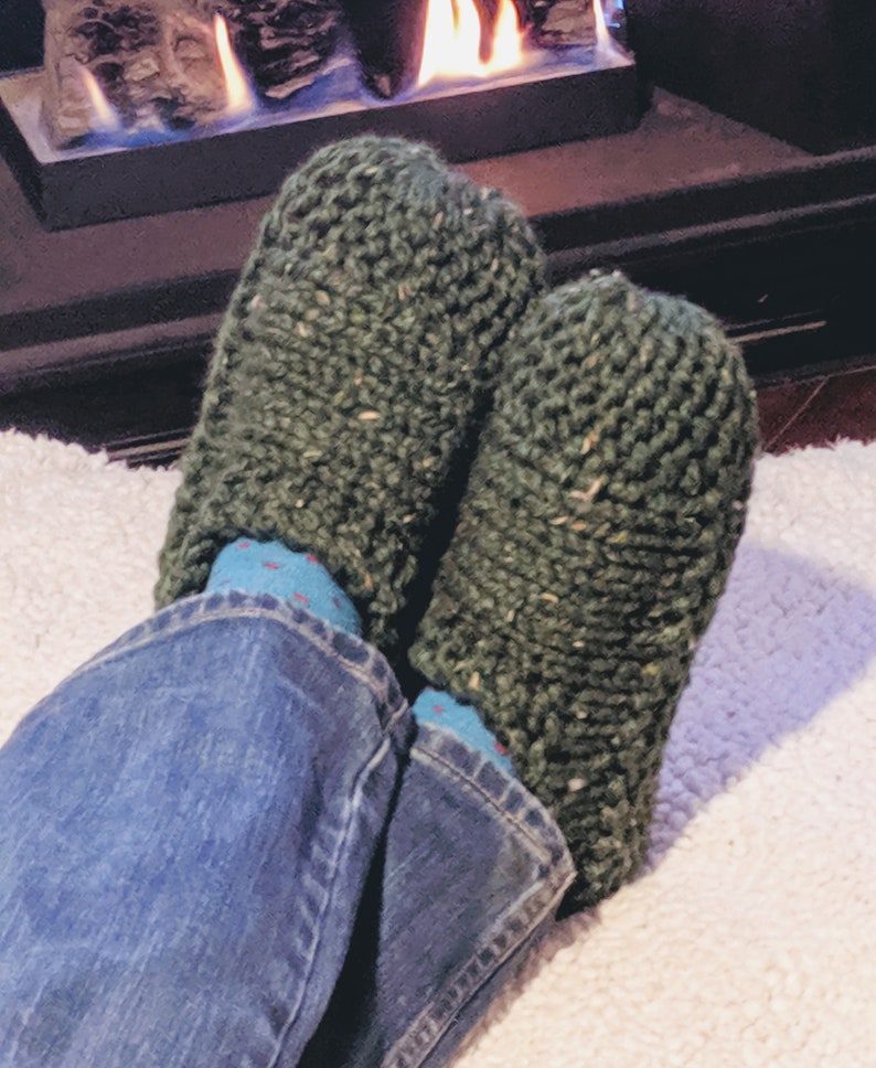 May include: A pair of green knitted slippers with a flecked texture. The slippers are worn by a person sitting in front of a fireplace.