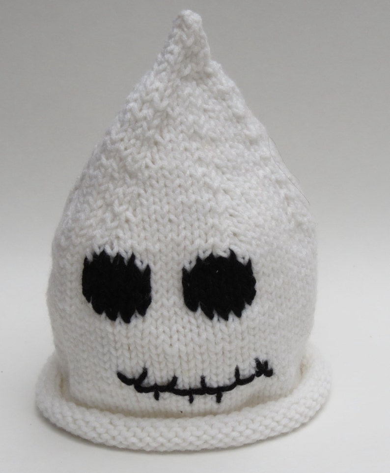 May include: White knitted ghost hat with black embroidered eyes and a stitched mouth.
