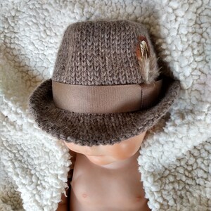 Peut inclure: Un chapeau fedora en tricot marron avec un ruban marron et une petite plume.