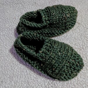 May include: A pair of dark green knitted slippers with a textured surface.