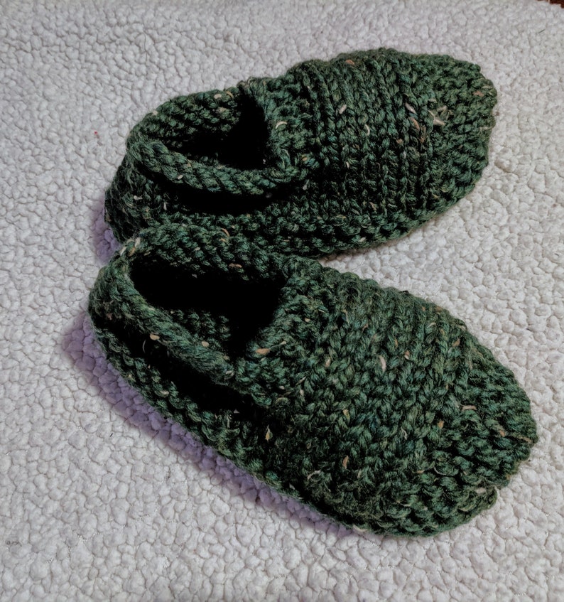 May include: A pair of dark green knitted slippers with a textured surface.