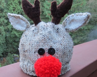 May include: A knitted reindeer hat with brown antlers, white ears, black button eyes, and a red pom-pom nose.