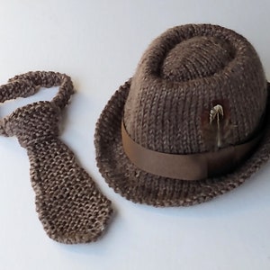 Peut inclure: Un chapeau fedora en tricot marron avec un ruban marron et une petite plume marron en guise d'accent. Une cravate en tricot marron assortie est &eacute;galement incluse.